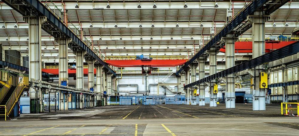 An industrial plant bay running the length of the building, overhead cranes on the rails and marked lanes across the floor.