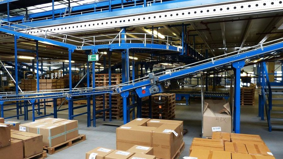 Powered roller conveyor lines running through a distribution hall with cartons staged on pallets alongside.